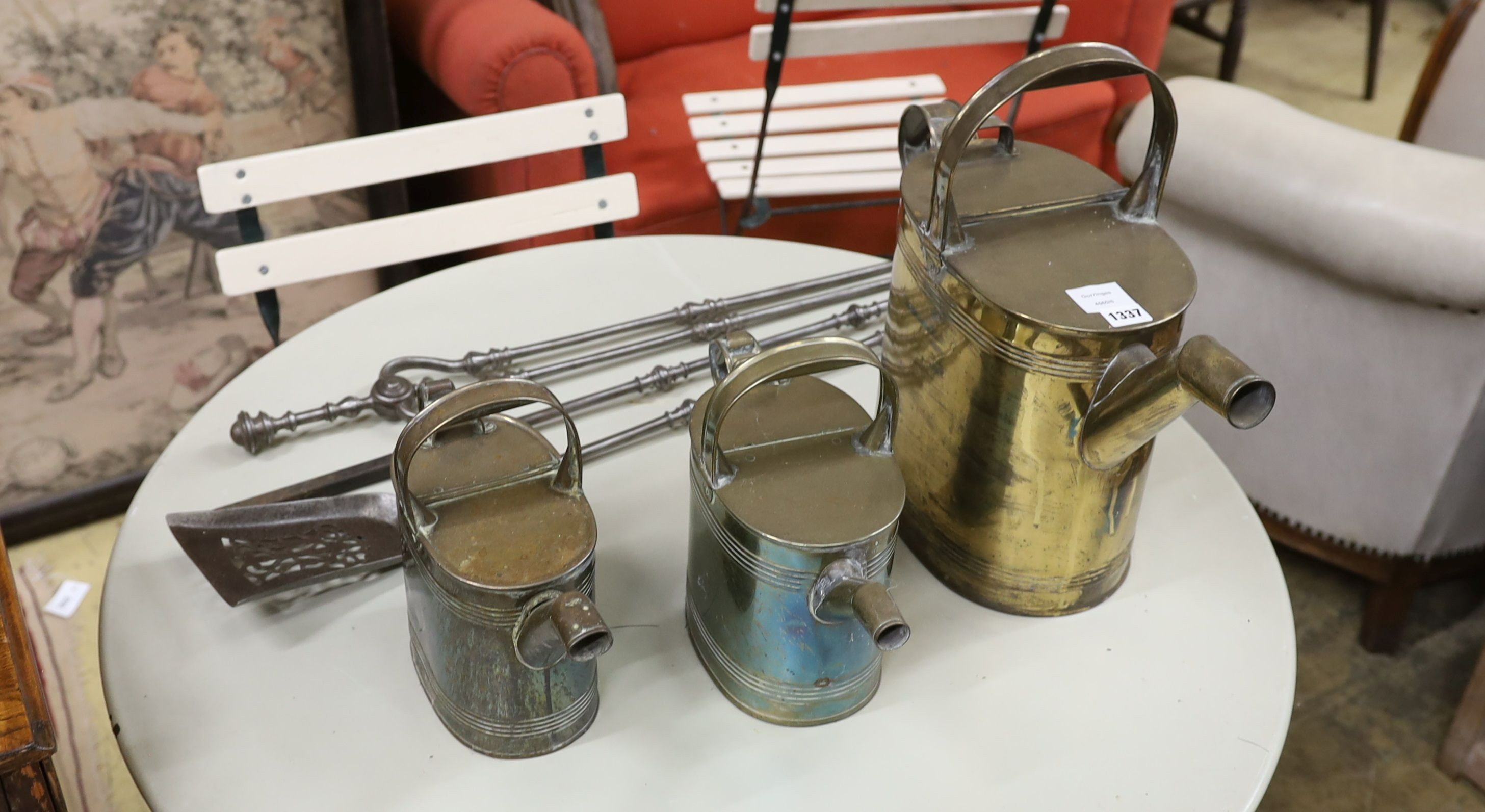 Three graduating brassed metal watering cans, largest height 40cm, together with a set of cast iron fire implements